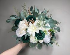 a bouquet of white and green flowers in someone's hand on a gray background