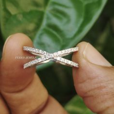 a person is holding a diamond ring in their left hand and there are green leaves behind them