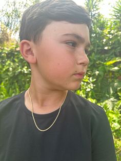 a young boy wearing a black shirt and gold necklace