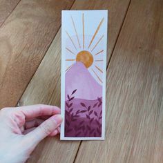 someone is holding up a card with the image of a mountain and sun on it