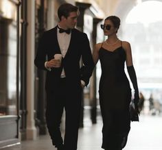 a man and woman dressed in black walking down the street with one holding a coffee cup