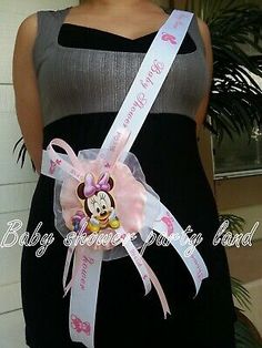 a pregnant woman wearing a pink minnie mouse ribbon around her waist and holding a mickey mouse sash