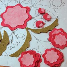 some paper flowers are sitting on a piece of white paper with pink and brown trim