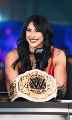 the woman is smiling while holding up her wwe championship belt in front of a microphone