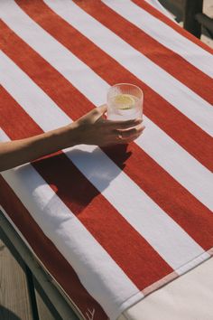 a person holding a glass on top of a red and white striped table cloth at an outdoor dining area