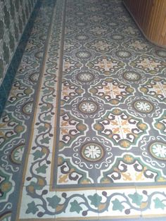 an ornate tiled floor in a bathroom next to a bathtub and toilet paper dispenser