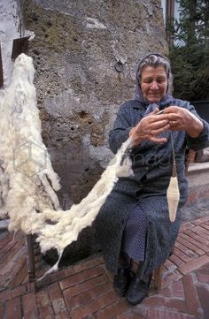 an old woman sitting on a bench next to a pile of yarn