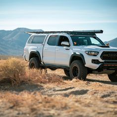 a white truck parked on top of a dry grass covered field with mountains in the background