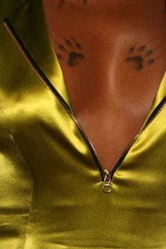 a woman with tattoos on her chest is wearing a gold dress and has an open zipper