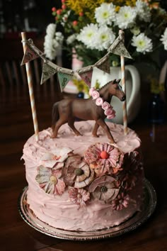 a pink cake decorated with flowers and a horse figurine sitting on top of it