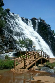 a wooden bridge over a small stream in front of a waterfall