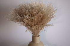 a vase filled with dry grass on top of a white tablecloth covered table cloth