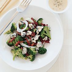 a white plate topped with broccoli covered in feta cheese and sauces