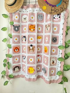 a crocheted baby blanket with animals on it and two hats hanging from the wall