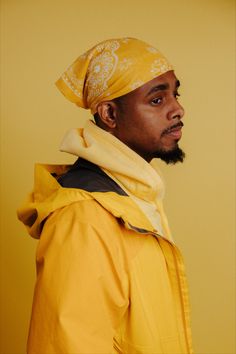 a man in a yellow jacket and bandana looks off to the side with his head tilted