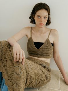 a woman sitting on the floor with her legs crossed and wearing a brown knitted top