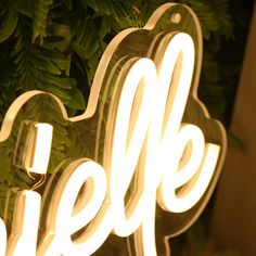 a neon sign with the word hello written on it in front of some plants and leaves