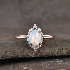 a white opal and diamond ring sitting on top of a piece of stone with a black background