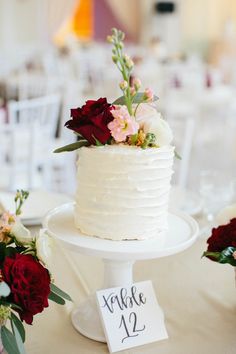 a white wedding cake with flowers on the top and table number displayed in front of it