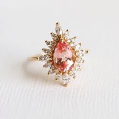 a pink and white diamond ring sitting on top of a white surface with gold accents