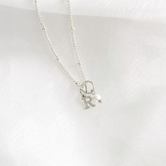 This stunning dainty letter necklace with pearl charm is perfect for anyone looking for understated elegance. The necklace features a delicate silver chain that holds a small, exquisite pearl charm and a capital letter of your choice.  ♡ Handcrafted in our Sydney Studio ♡ Natural Freshwater Pearl ♡ 925 Sterling Silver Plated ♡ Water Resistant ♡ 5mm Charm  PACKAGING: All of our items are carefully packed into a white jewellery box topped with a delicate white satin bow. Our shipping bags are beig Silver Initial Pendant Necklace With Pearl Charm, Silver Necklace With Initial Pendant And Pearl Charm, Sterling Silver Charm Necklace With Pearl Pendant For Anniversary, Sterling Silver Pearl Charm Necklace, Delicate Silver Initial Pendant Name Necklace, Delicate Silver Initial Pendant Necklace, Silver Charm Necklace With Initial Pearl Pendant, Everyday Sterling Silver Necklace With Pearl Charm, Dainty Jewelry With Pearl Charm Initial Pendant