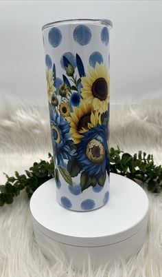 a vase with sunflowers painted on it sitting on a white stand next to some plants