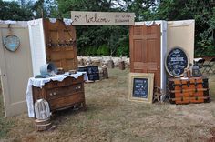 an outdoor display with antique furniture and chalkboard signs on it's sides, in the grass