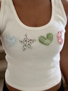 a woman wearing a white tank top with hearts and stars embroidered on the side,