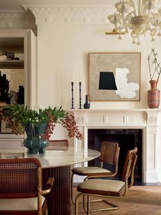 a dining room table with chairs and vases on it in front of a fireplace