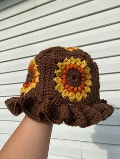 a crocheted brown hat with sunflowers on the brim is being held by a person