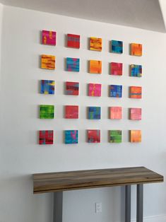 a wooden table sitting in front of a white wall with many colorful paintings on it