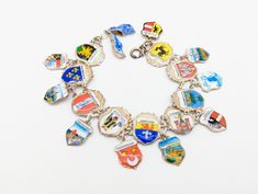 A wonderful vintage 925 and 800 silver enameled charm bracelet commemorating European travel, mostly German. The main bracelet is made of 9 shield shaped charms, all marked 925. There are nine smaller charms dangling from the main bracelet. Most are marked 835.  The end has two enameled sterling silver Dutch shoe charms. Locations include: Heidelberg, Wiesbaden, Kaiserslautern, Schloss Linderhof, Igls, Monessee Talsphere, Munchen, Madurodam, Darmstadt, Berg Richenstein, Pirmasens, Baumholder, Ga Vintage Silver Jewelry With Coat Of Arms, Silver Enamel Jewelry Souvenir, Silver Enamel Jewelry With Vintage Charm, Silver Enamel Charm Bracelet, Silver Enamel Charm Bracelets, Silver Charm Bracelets With Enamel, Silver Enamel Bracelets With Charms, Silver Enamel Bracelet, Travel Charm Bracelet