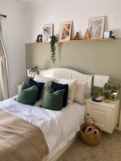 a white bed with green pillows and some pictures on the wall above it in a bedroom