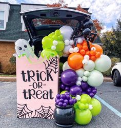 a trunk or treat sign with balloons and decorations in front of a halloween themed car