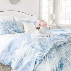 a bed with blue and white comforter in a bedroom next to a window filled with pink flowers