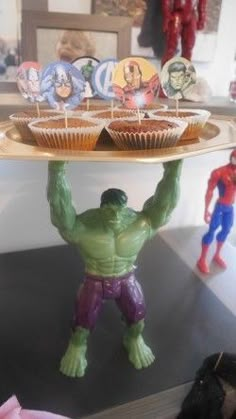 the hulk cupcakes are being held by two toy figurines on a cake plate