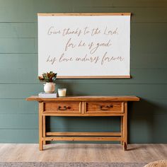 a wooden table sitting in front of a wall with a sign above it that says, give thanks to the lord for he is good his love always forever