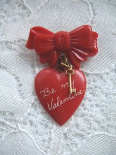 a red heart with a key hanging from it's side on a lace covered surface