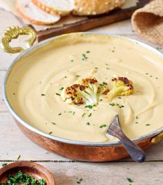 there is a bowl of soup with broccoli in it and bread on the side