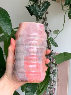 a person holding up a pink and purple drink in front of a plant with green leaves