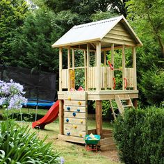 a wooden play set in the middle of a garden with climbing wall and ladders