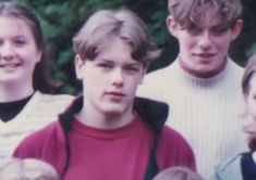 a group of young people standing next to each other in front of some green trees