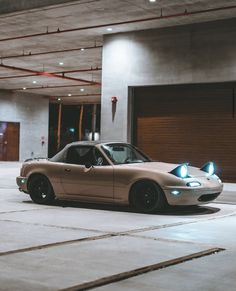 a tan sports car parked in an empty parking garage with its hood up and lights on