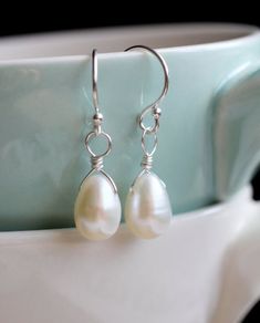 two white pearls are hanging from silver earwires in front of a blue cup