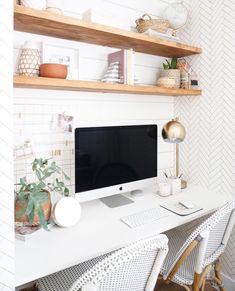 a white desk topped with a computer monitor next to a shelf filled with potted plants