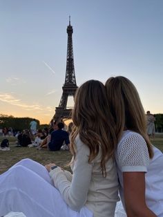 two women sitting on the ground in front of the eiffel tower at sunset