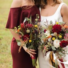 two bridesmaids in burgundy dresses holding bouquets of flowers and greenery on their wedding day