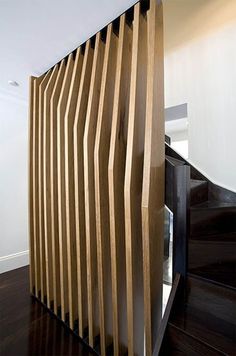 an unusual wooden partition in the middle of a room with dark wood flooring and white walls