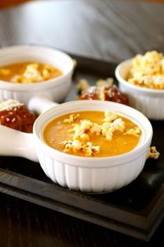 three bowls of soup on a tray with spoons