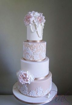 a three tiered wedding cake with white and pink flowers on the top, sitting on a table